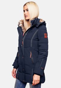 Cămașă puffer de marină cu glugă căptușită cu blană, design matlasat, buzunare cu fermoar și detalii din piele maro pe mânecă.