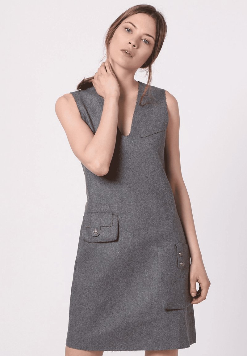 Vestido gris sin mangas con escote en V, hecho de fieltro, que cuenta con dos bolsillos frontales con botones y un diseño minimalista. Textura suave en todo el vestido.