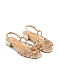 Sandalias metálicas doradas con tiras trenzadas, puntera abierta y un tacón bajo. Textura suave con un ligero brillo; correa ajustable en el tobillo.