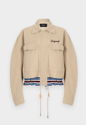 Jachetă bej scurtă, cu două buzunare la piept, fermoar frontal și tiv elastic cu dungi albastre, albe și roșu închis. Broderie cu logo-ul brandului pe piept.