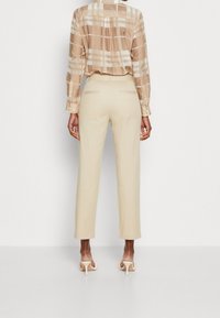 Beżowe spodnie o kroju prostym z tylnymi kieszeniami. Połączone z jasną koszulą w kratę z długim rękawem w neutralnych odcieniach.