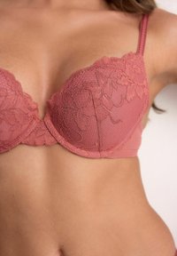 Záber na ženský trup v práškovo ružovej čipkovanej podprsenke s kvetinovými vzormi a nastaviteľnými ramienkami.