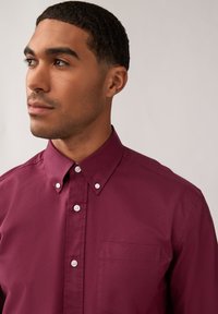 Camicia button-up bordeaux in cotone, con taschino frontale, colletto a punta e bottoni bianchi sulla pattina e sul colletto.