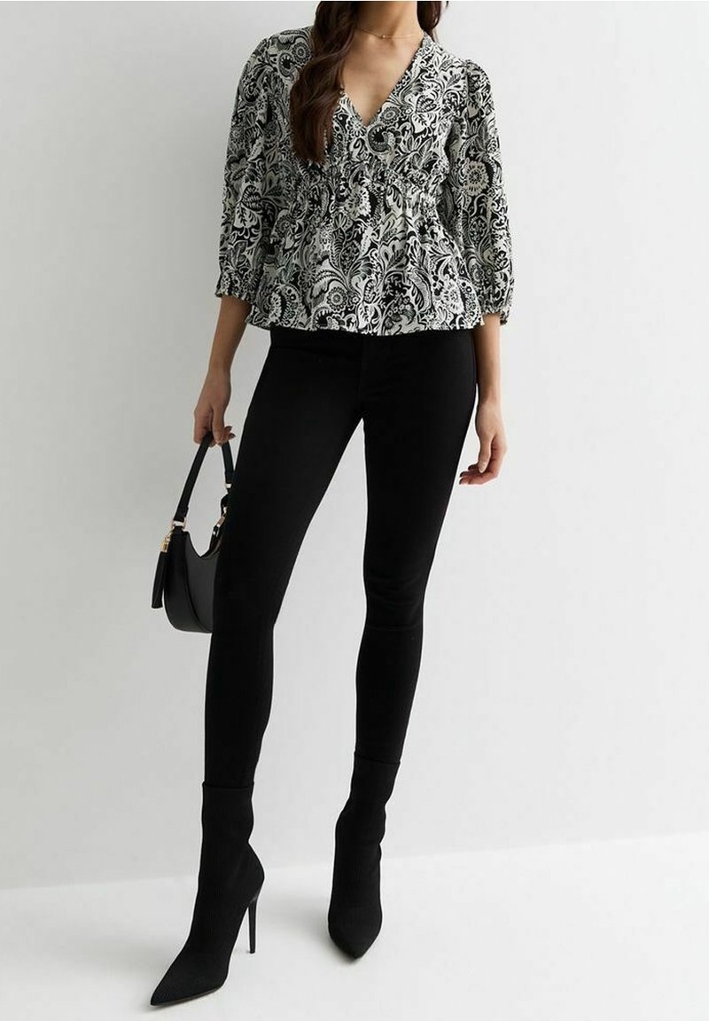 Blouse à motifs noir et blanc avec un col en V, des manches trois-quarts et une taille froncée, associée à un jean skinny noir et des talons noirs.