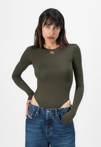 Olive green long-sleeve bodysuit with high-cut sides and small logo detail at the neckline, paired with blue denim high-waisted jeans.