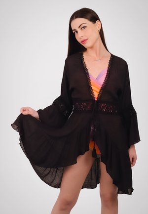 Kimono in chiffon nero con maniche a sbuffo, apertura frontale e dettagli in pizzo intricati. Tessuto leggero con design a cascata e accentuazioni con frange.