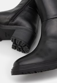 Czarne skórzane botki na kostkę o gładkim wykończeniu, z bocznym zamkiem błyskawicznym, blokowym obcasem oraz teksturowaną gumową podeszwą z wzorami antypoślizgowymi.