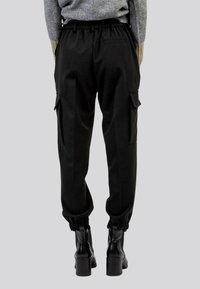Pantaloni cargo neri con vita elastica, tasche laterali e polsini regolabili; abbinati a stivali neri con tacco. Tessuto in misto cotone.