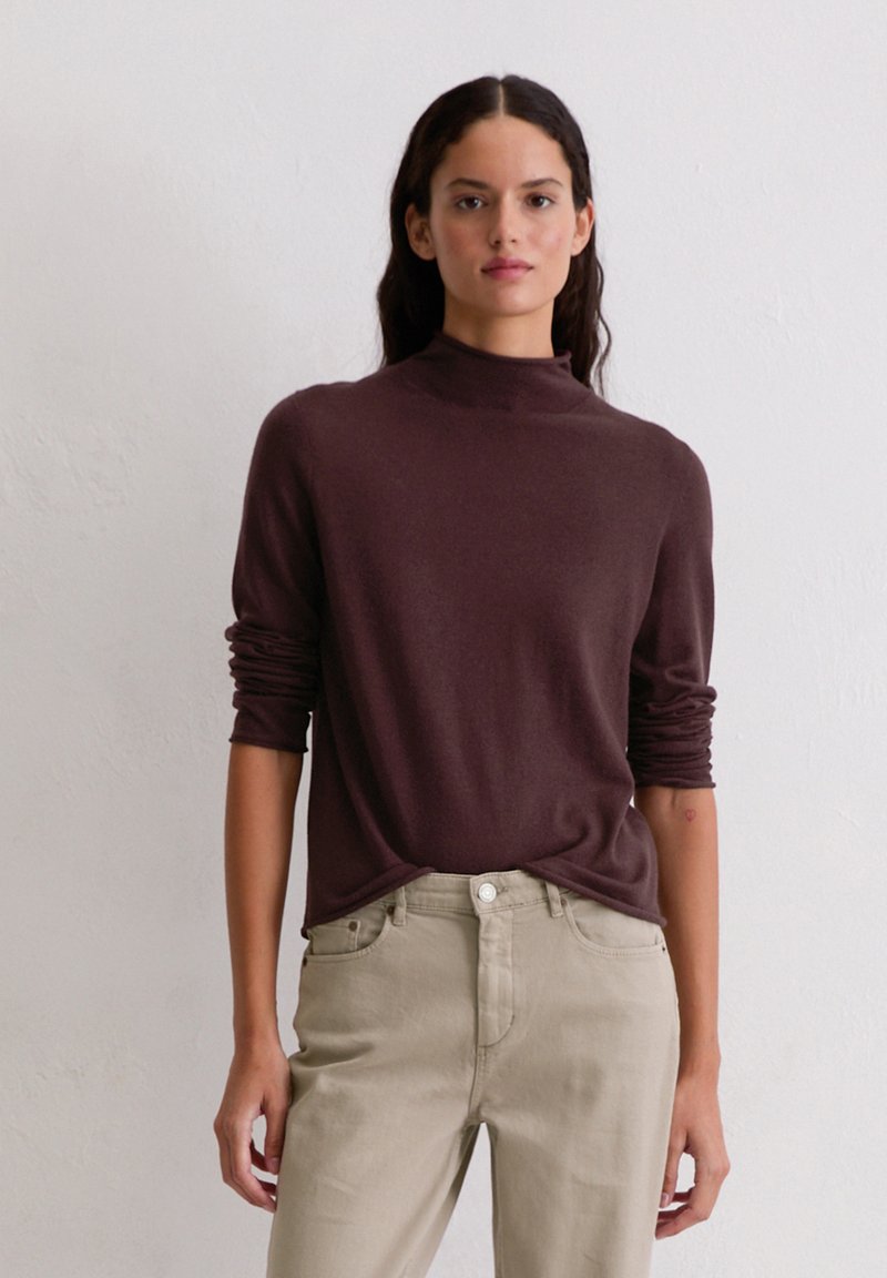 Bruine, lange mouwen trui met een opstaande kraag, gemaakt van een zachte stof, gecombineerd met lichtbeige denim jeans. Eenvoudige, aansluitende silhouet.