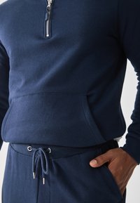 Marineblå fleecepullover med kvart-zip hals, med en framficka och matchande joggers med dragsko och metallaccenter.