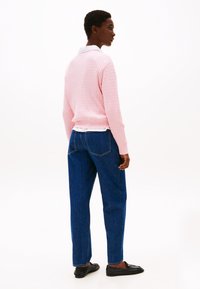Pull en tricot rose clair avec un motif texturé, associé à un jean taille haute bleu foncé et des mocassins noirs, vu de dos.