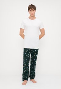 Tricou alb cu mânecă scurtă asociat cu pantaloni de pijama verzi, având un model cu diferite băuturi și obiecte în culori vii.