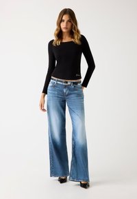 Top negro de manga larga con escote cuadrado, combinado con jeans de pierna ancha de color azul claro con un lavado desvanecido, herrajes plateados y un cinturón.