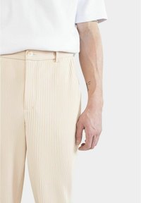 Beige randiga byxor i vävd tyg, med knappstängning och fickor. Slät textur med en skräddarsydd passform.
