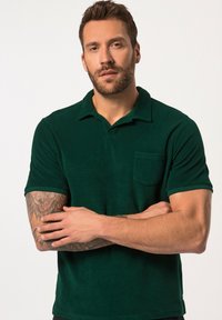 Polo verde realizzato in materiale morbido, con collo classico, maniche corte e taschino sul petto. Superficie texturizzata con colore uniforme.