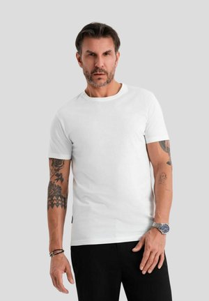 Weißes Baumwoll-T-Shirt mit Rundhalsausschnitt, kurzen Ärmeln, taillierter Passform und dezenten Nähten, kombiniert mit schwarzen Hosen und einer Uhr.