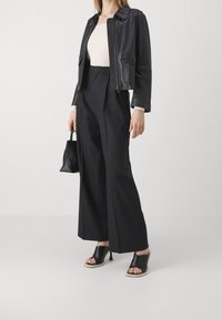 Sorte læder cropped jakke, cremet ribbet top, højtaljede sorte brede bukser, sorte åbne mules, holder en lille sort taske.