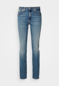 Jean slim bleu avec légère décoloration sur l'avant des cuisses, style cinq poches, fermeture bouton et passants de ceinture.