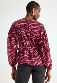 Vaaleanpunainen ja viininpunainen kuviollinen paita, jossa on rento istuvuus, pitkät hihat, kiristetty vyötärö ja teksturoitu kangas, jossa on hienovarainen aallonmuotoinen kuvio.