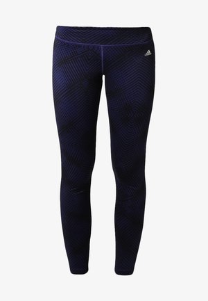 Femme marchant, portant un débardeur noir Adidas, des leggings bleu foncé à motifs, et des baskets noires Adidas.