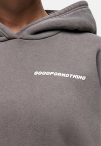 Felpa grigia realizzata in morbido tessuto, con un grande logo bianco "GOODFORNOTHING" sulla parte anteriore. Il design include un classico cappuccio con lacci.