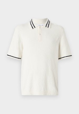 Lühikeste varrukatega polo särk kreemja tekstuuriga kangast, millel on kudumiskrae kahe musta triibuga ja kolme nupuga kinnitamine.