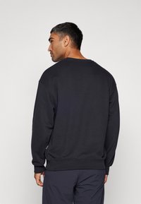 Felpa nera con collo rotondo e maniche lunghe, caratterizzata da una vestibilità comoda e una texture liscia. Il design sul retro è semplice, senza ulteriori dettagli.