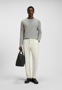 Maglione lavorato a maglia grigio chiaro, pantaloni sartoriali bianco sporco, scarpe in pelle nere e una borsa in pelle nera. Linee semplici e pulite con texture morbide.