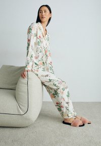 Floral-patterned pajama set in lightweight fabric; features long sleeves and pants. Fuzzy pink slip-on slippers with black soles.
