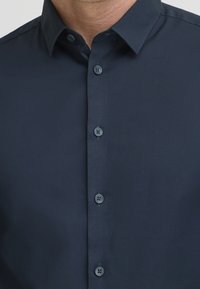 Donkerblauwe overhemdenkleding van gladde stof, met een puntkraag en zes knopen, voorzien van een subtiele glans en stiksel.details.
