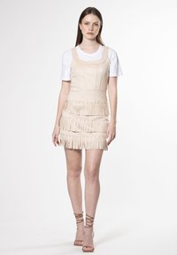 Vestido de ante beige con escote cuadrado y múltiples capas de flecos, combinado con una camiseta blanca y tacones de tiras beige.