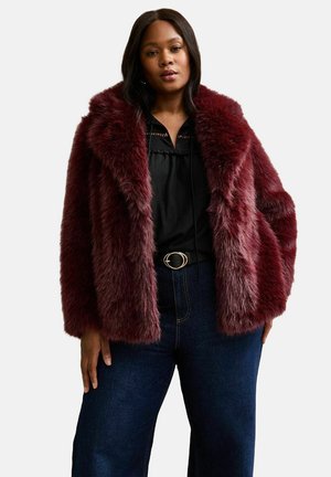Giacca in pelliccia sintetica bordeaux con colletto ampio, abbinata a una blusa nera e jeans in denim scuro a vita alta. Texture morbida e vestibilità rilassata.