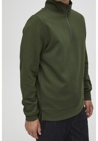 Mörkgrön zip-up fleece-pullover med hög krage, sidofickor och ribbade ärmslut. Mjuk textur och strömlinjeformat design.