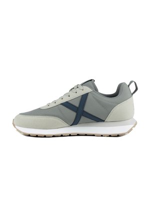 Zapatilla gris y beige claro con franja azul transversal, suela blanca, cordones delante y lengüeta trasera, vista desde el lado derecho.