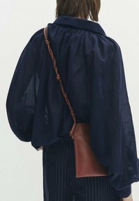 Granatowa, luźna bluzka z szerokimi rękawami, zestawiona z spodniami w drobną prążek i małą, brązową skórzaną torebką na ramię.