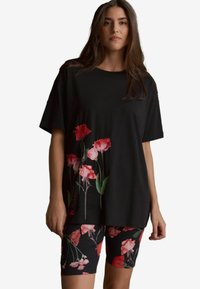 Zwarte oversized t-shirt met bloemenontwerp in tinten van roze en rood, gecombineerd met zwarte shorts met een bijpassend bloemenpatroon.