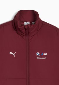 Veste matelassée bordeaux avec col haut, fermeture éclair frontale, logo Puma blanc et marquage BMW Motorsport. Texture lisse, matériau isolant.