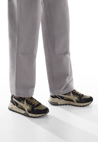 Sneaker nere e verde olivo con una suola crema maculata, caratterizzate da un logo prominente, materiali testurizzati e un design con lacci.