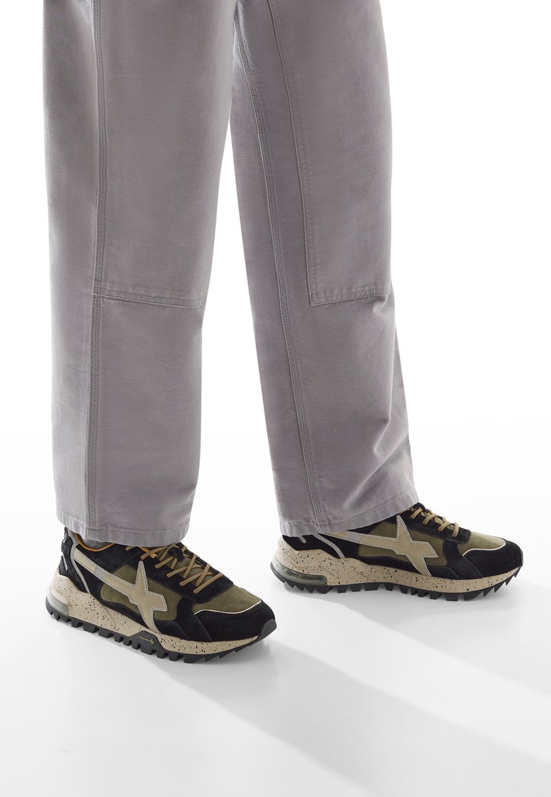 Sneaker nere e verde olivo con una suola crema maculata, caratterizzate da un logo prominente, materiali testurizzati e un design con lacci.