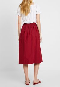 Czerwona spódnica za kolano z elastycznym paskiem i marszczonym fasonem. Połączona z białą, krótkim rękawem bluzką z falbankami na krawędziach.