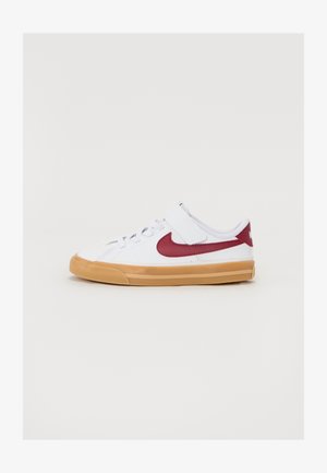 Balti sportiniai bateliai su raudonu Nike swoosh, tekstūruota audinio viršutinė dalis, reguliuojama juosta ir guminis padas. Žemas profilis.