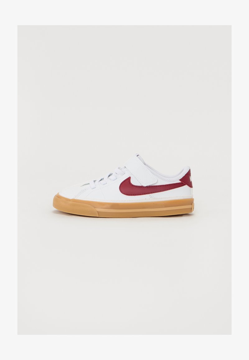 Bela atletska čevlja z rdečim Nike žigom, zgornji del iz teksturirane tkanine, nastavljiv trak in gumijast podplat. Nizkotehnološka zasnova.