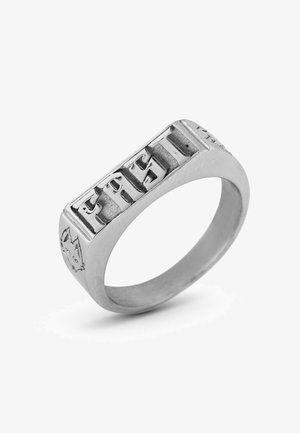 Ezüst gyűrű, melynek elülső oldalán domború "EAST" felirat található, oldalán részletes farkas mintával, sima és fényes felülettel.