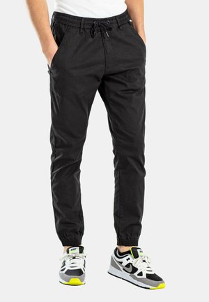 Schwarze, mit Kordelzug und elastischem Bund ausgestattete Hose mit Seitentaschen und elastischen Bündchen. Getragen mit schwarz-weißen Sneakern mit Neonakzenten.