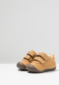 Scarpe in pelle marrone chiaro con doppie chiusure in velcro, punta arrotondata in gomma marrone e dettagli di cucitura a contrasto. Texture liscia con design robusto.
