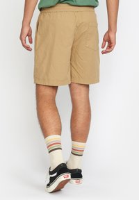 Khaki shorts met een elastische tailleband, zijzakken en een achterzak. Gecombineerd met gestreepte roomkleurige en bruine sokken en zwarte sneakers.