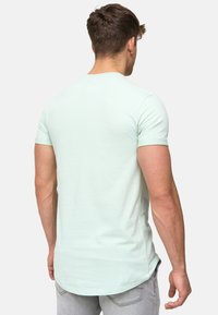 Helles grünes T-Shirt mit kurzen Ärmeln und rundem Ausschnitt, mit geradem Schnitt und leicht verlängertem Rückensaum, aus weichem Stoff gefertigt.