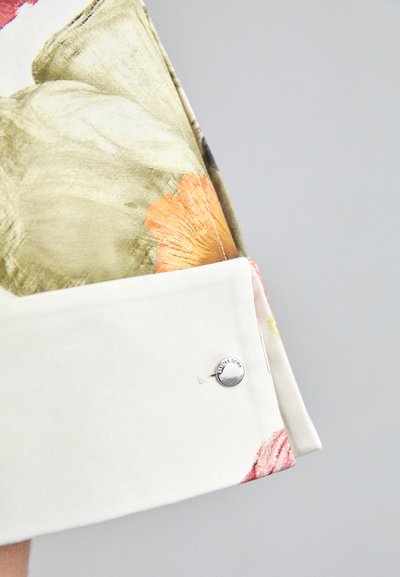 Blusa con estampado floral y puño blanco; tejido suave en tonos de verde, naranja y rosa. Botones de plata adornan el puño.