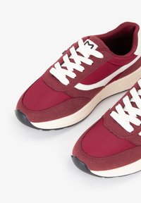 Sneaker bordeaux con tomaia in suede e tessuto, lacci bianchi, design atletico classico, punta arrotondata e suola in gomma nera a contrasto.