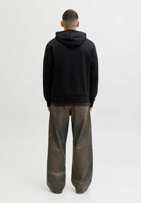 Sweatshirt noir à capuche avec une coupe décontractée, associé à un jean gris délavé à jambes larges affichant une subtile texture usée.